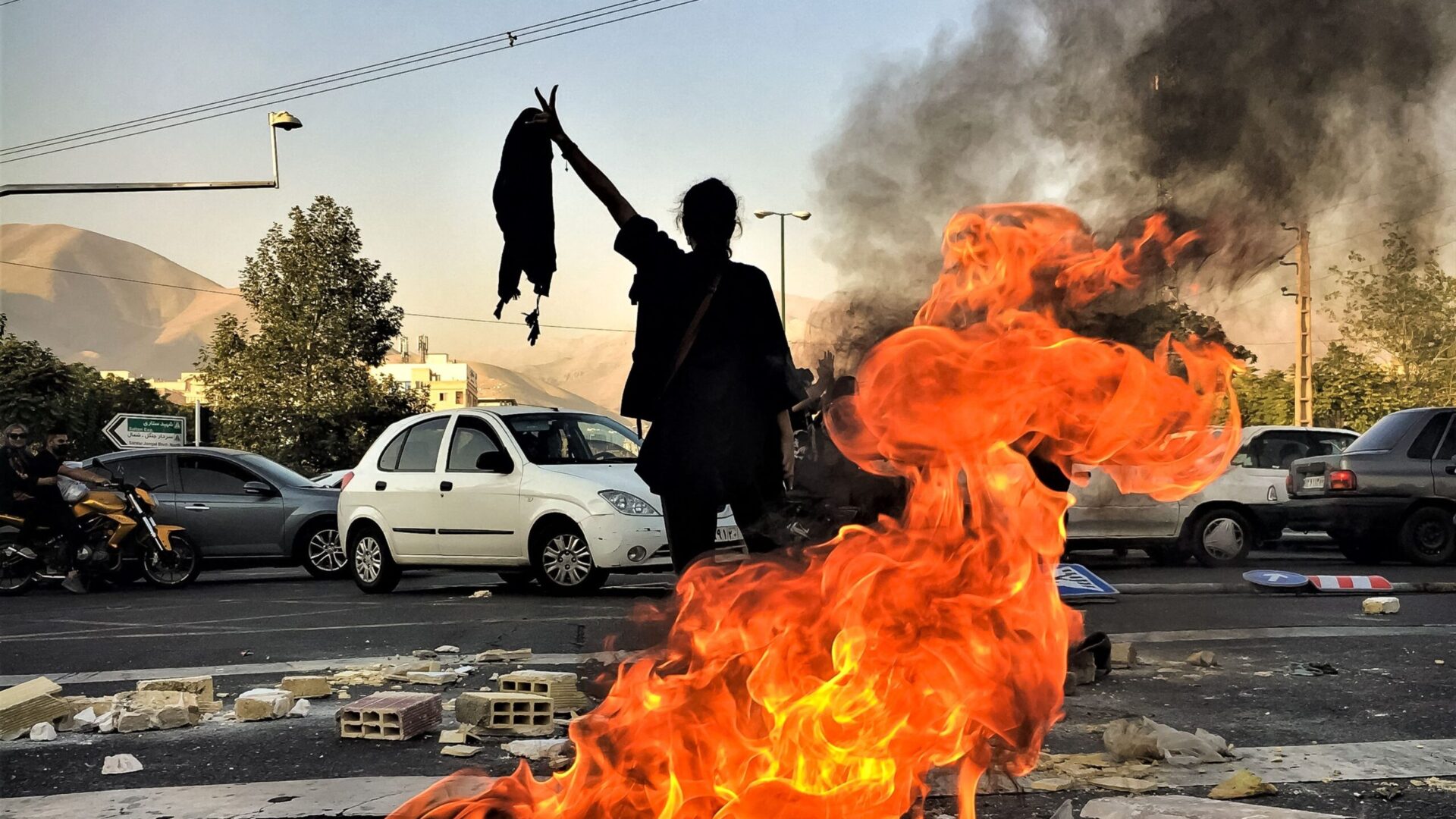 10/01/2022 Tehran, Iran. An Iranian woman without wearing a hijab flashes a victory sign near a burning tire during a protest near Punak square. The nationwide protests started after the death of Mahsa Amini, a 22-year-old girl who died under the custody of the Islamic Republic's Morality Police on September 16th, 2022 in Tehran. (Photo by Anonymous / Middle East Images / Middle East Images via AFP) (Photo by ANONYMOUS/Middle East Images/AFP via Getty Images)